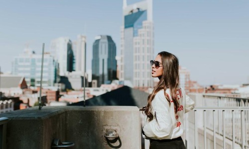 woman with sunglasses stands on a rooftop overlooking the city